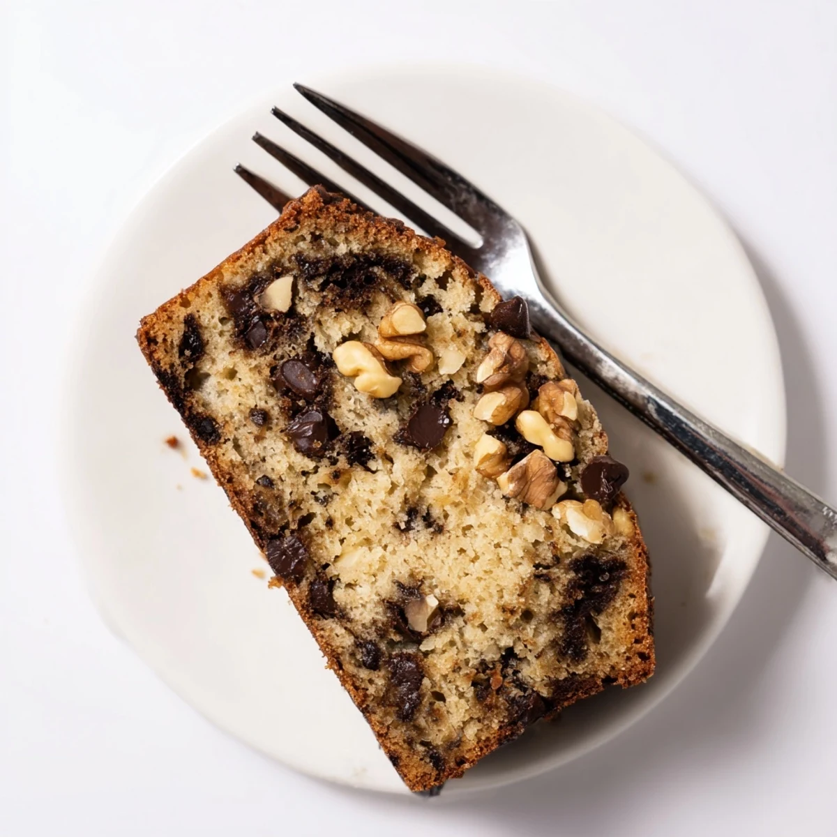 Warm slice of moist banana bread topped with melting butter on white plate