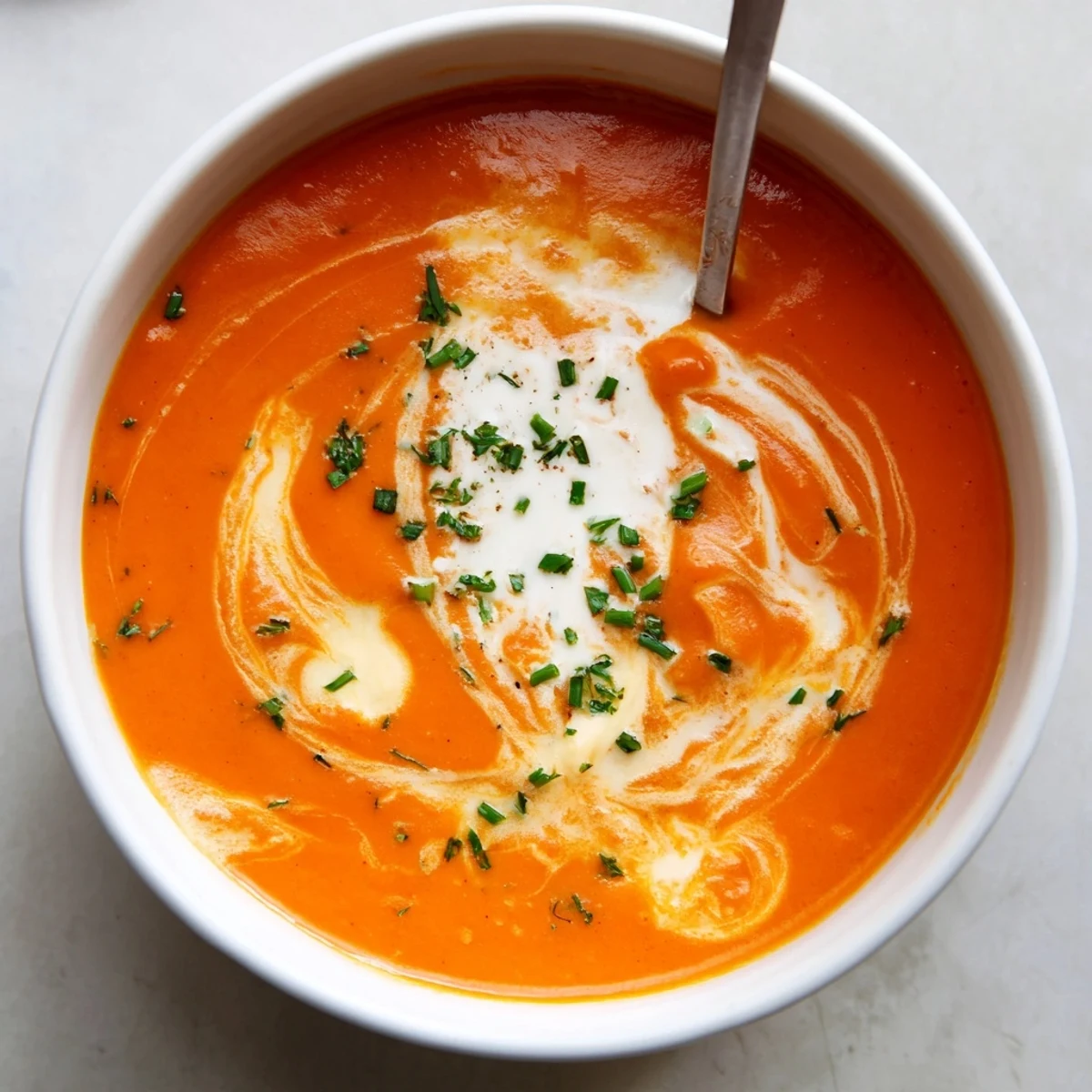 Creamy roasted red pepper Gouda soup garnished with fresh chives in a white bowl