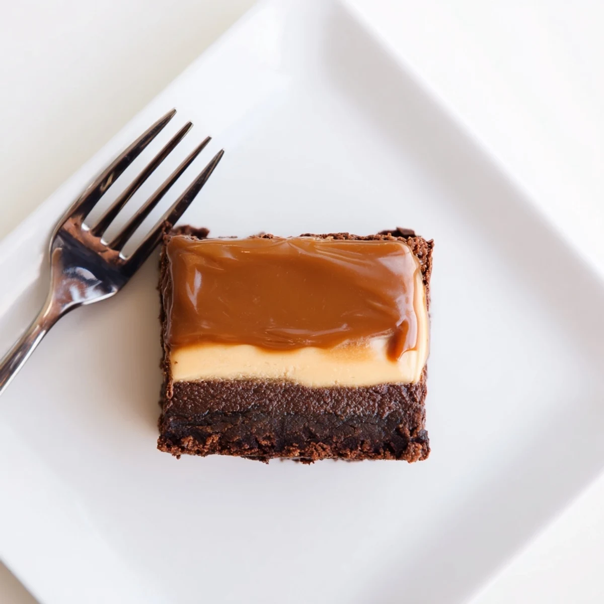 Square pan of caramel brownie cheesecake bliss topped with smooth melted caramel sauce