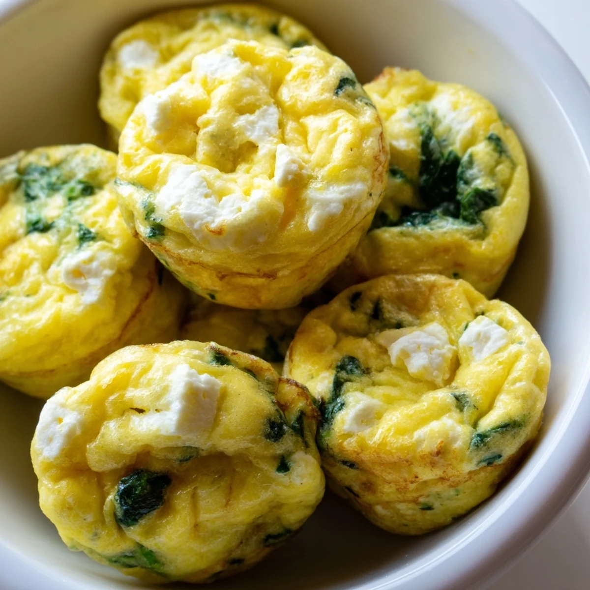 Fluffy spinach and feta egg muffins arranged on a white serving plate