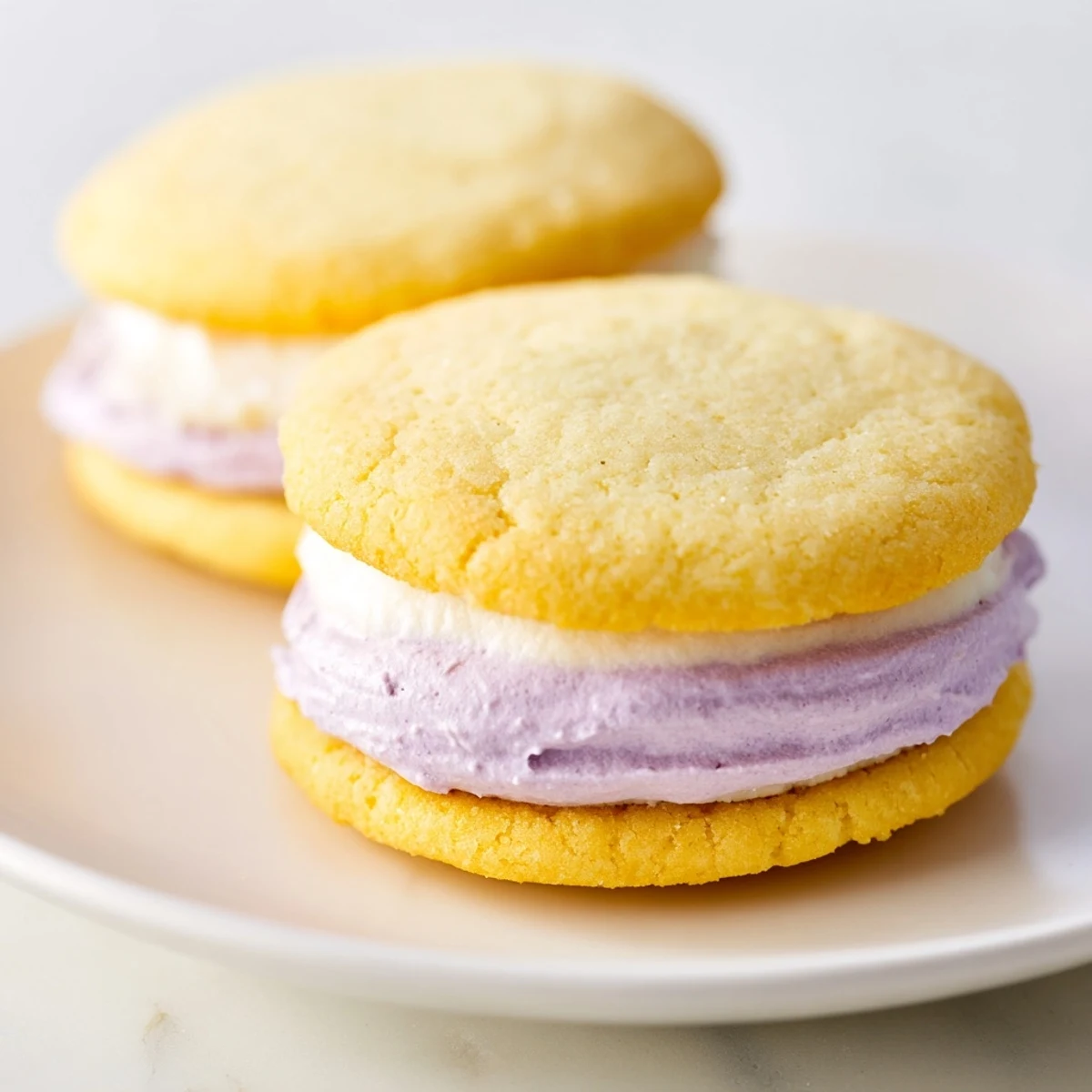 Soft pastel sugar cookie sandwiches with swirled buttercream filling on a rustic white plate