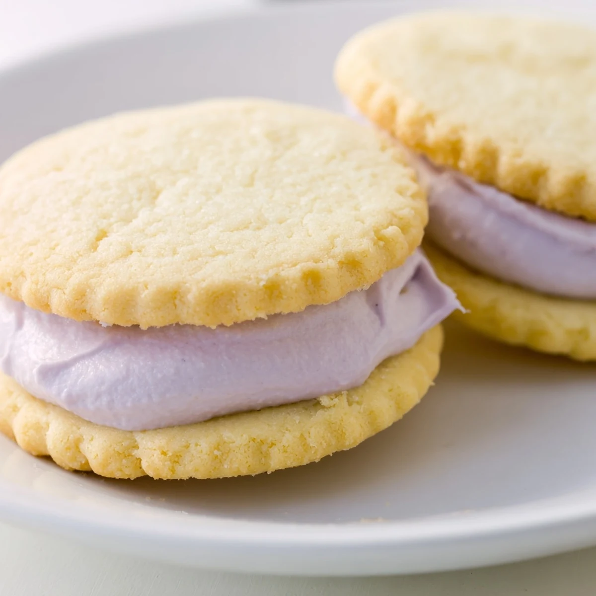 Delicate sugar cookie sandwiches showcase layers of pink blue and green buttercream frosting