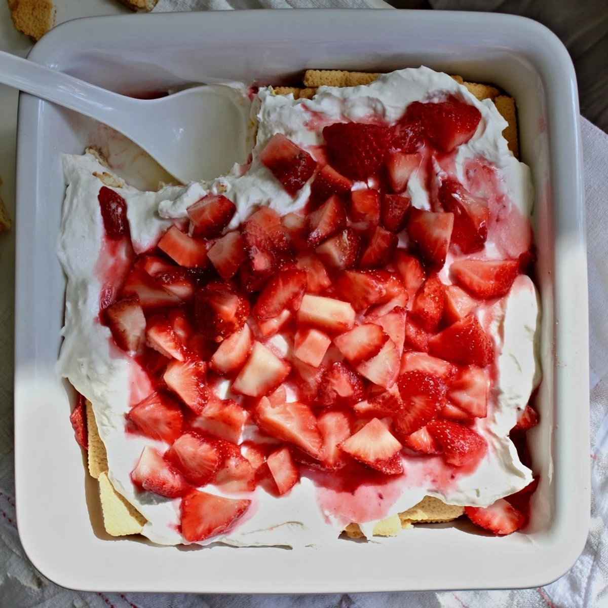 Square slice of no bake strawberry shortcake dessert showing white cream layers, red berries, and golden cookies