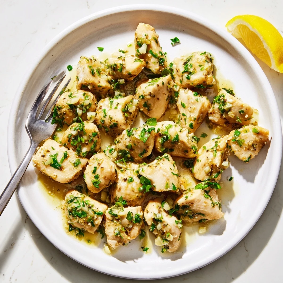 Tender chicken pieces simmering in rich garlic butter sauce with parsley and lemon wedges