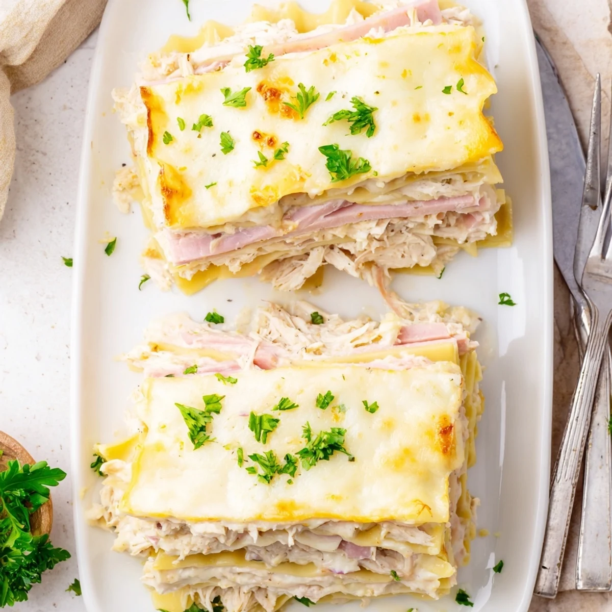 Sliced chicken cordon bleu lasagna on a white plate showcasing creamy béchamel and shredded Swiss layers