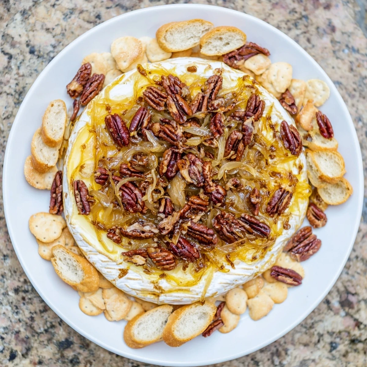 Golden wheel of baked brie oozing with sweet caramelized onions and toasted pecans on a wooden serving board