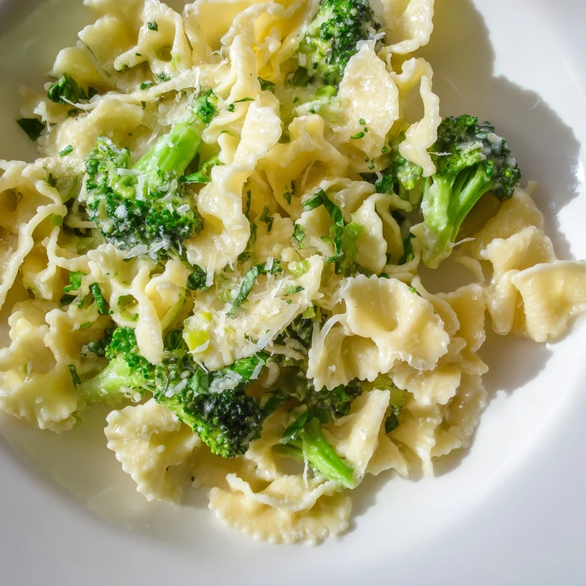 Steaming plate of Mafaldine Pasta Limone Broccoli topped with fresh herbs and golden melted cheese