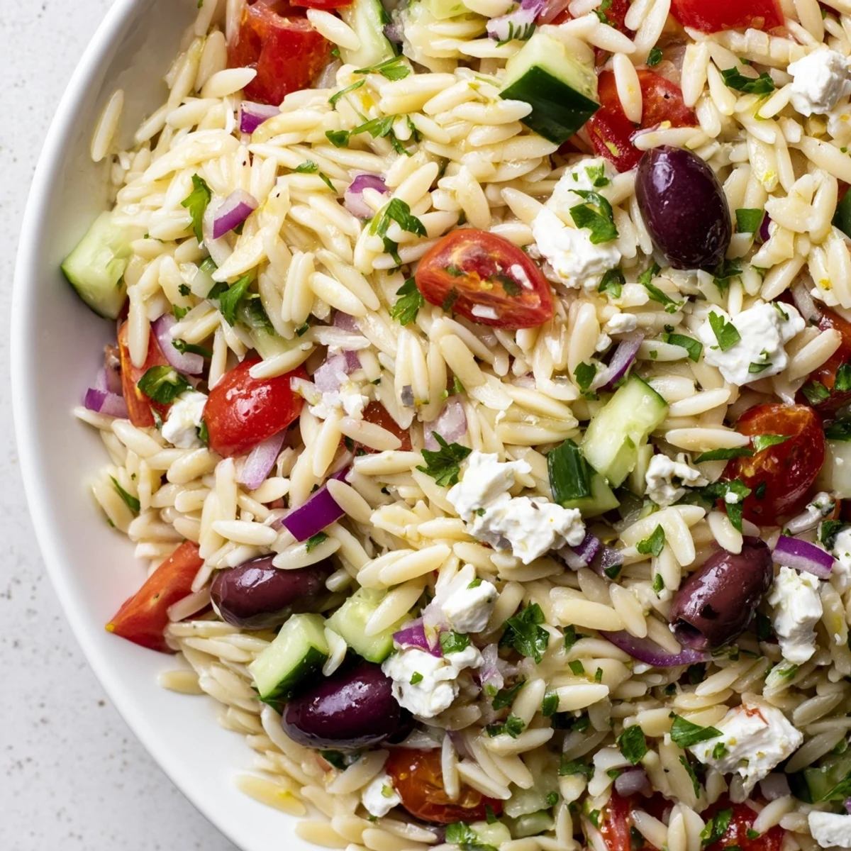 A colorful Mediterranean Orzo Pasta Salad in a rustic bowl topped with crumbled feta cheese
