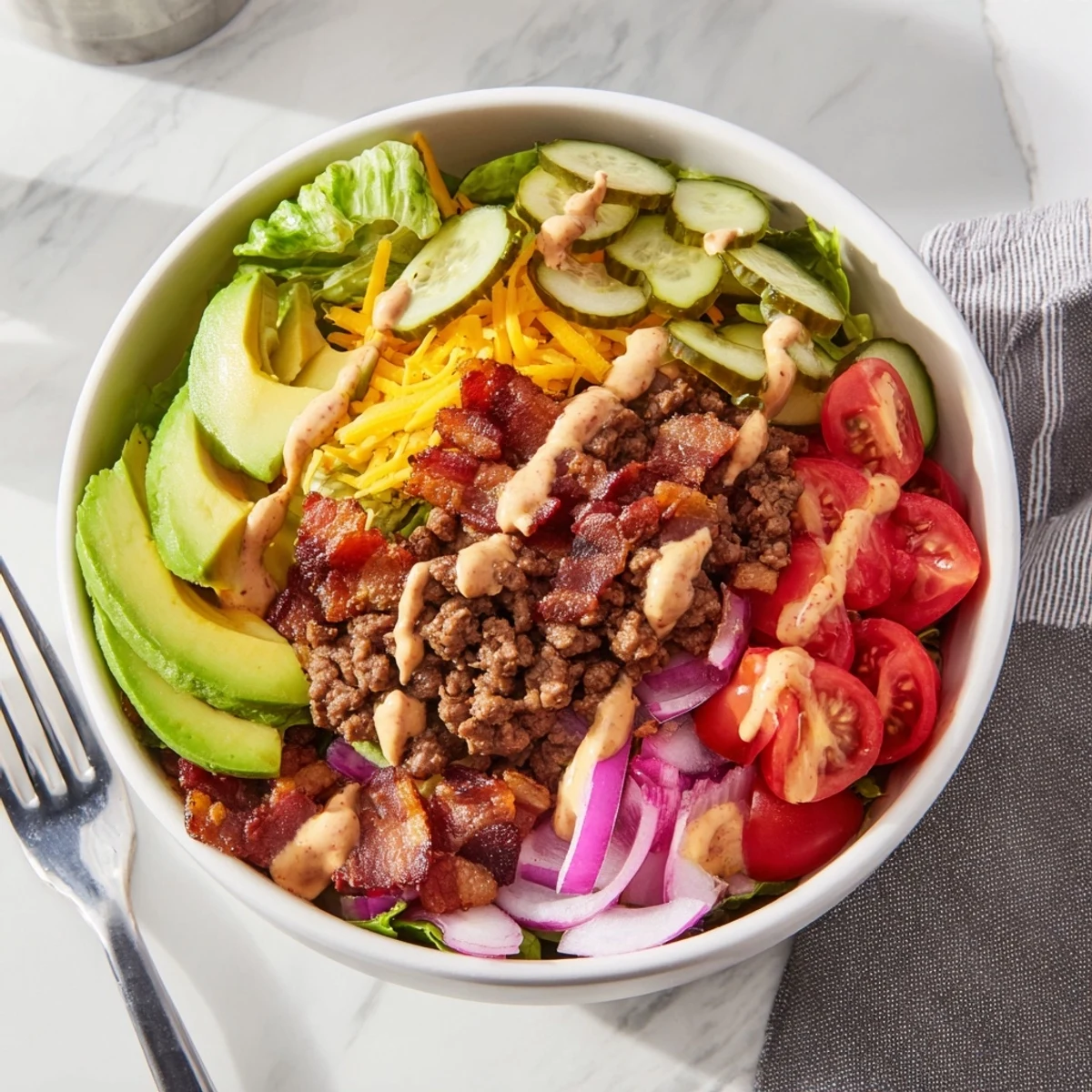 Vibrant burger bowl layered with juicy ground beef, tangy pickles, tomatoes, and a creamy white sauce.