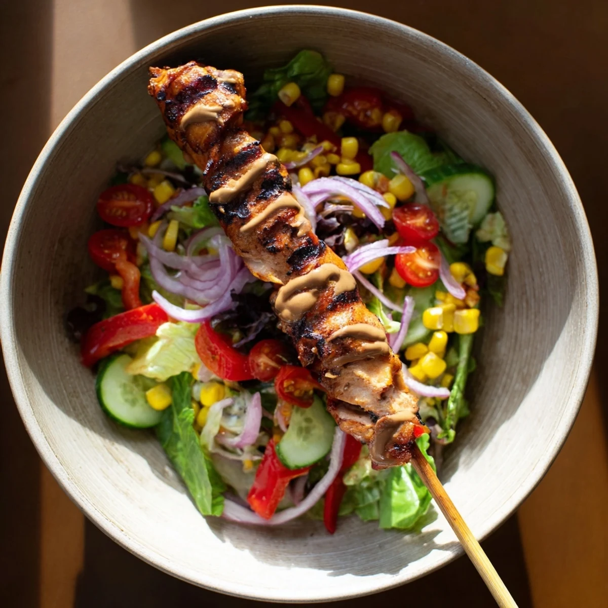 Summery BBQ chicken skewer salad with charred chicken, sweet corn, and cherry tomatoes on greens.