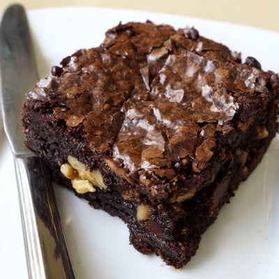 Rich ultimate brownies dusted with cocoa powder, served on a rustic white plate