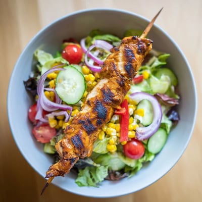 Delicious BBQ chicken skewer salad served fresh with tangy dressing and crunchy red bell peppers.